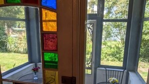 A conservatory with a glass door featuring colorful stained glass panels, a small table with a vase of flowers, and a view of a garden outside. - Turnbridge Manor (Denton)