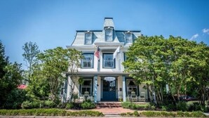 A two-story house with a gabled roof, a front porch, and a flag. - Turnbridge Manor (Denton)