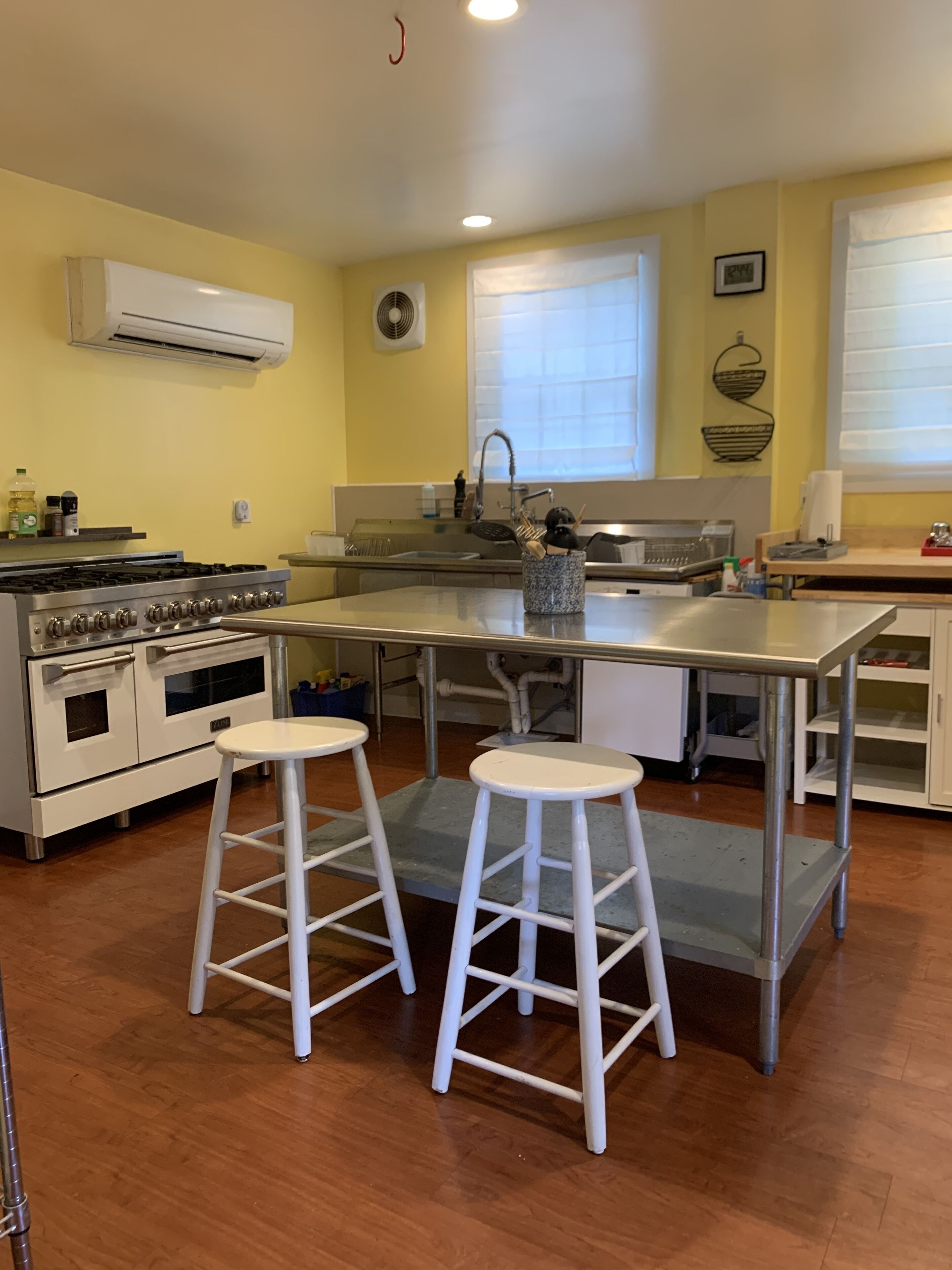 A kitchen with a central island, white stools, a stove, and a sink.