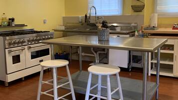 A kitchen with a central island, white stools, a stove, and a sink.