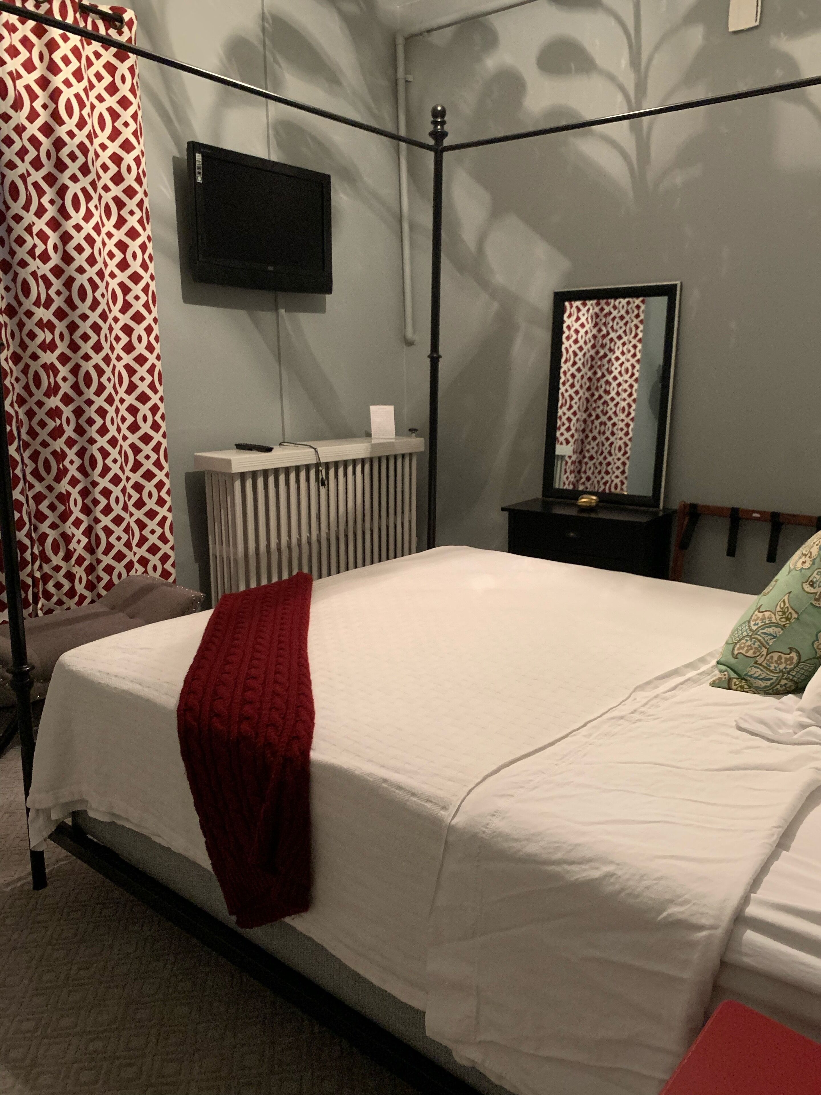 Een slaapkamer met een bed, een radiator, een aan de muur bevestigde televisie en een spiegel.