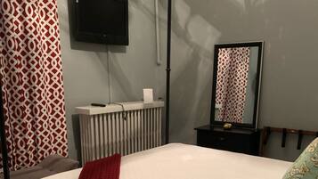 Een slaapkamer met een bed, een radiator, een aan de muur bevestigde televisie en een spiegel.