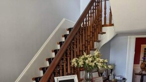 A wooden staircase with a white railing, a welcome sign, and a vase with flowers on a console table. - Turnbridge Manor (Denton)