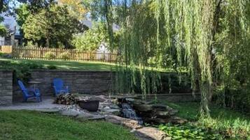 Ein Garten mit einem kleinen Teich, einer Holzterrasse und einer Trauerweide.
