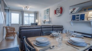 A dining area with a table set for four, a sofa, and a wicker chair. - Trewent Park - 2 Bed - Freshwater East (Pembroke)