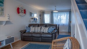 A living room with a brown leather sofa, a wicker chair, and a blue rug. - Trewent Park - 2 Bed - Freshwater East (Pembroke)