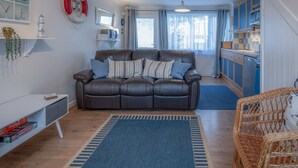 A modern living room with a brown leather sofa, a blue rug, and a kitchen area with blue cabinets. - Trewent Park - 2 Bed - Freshwater East (Pembroke)