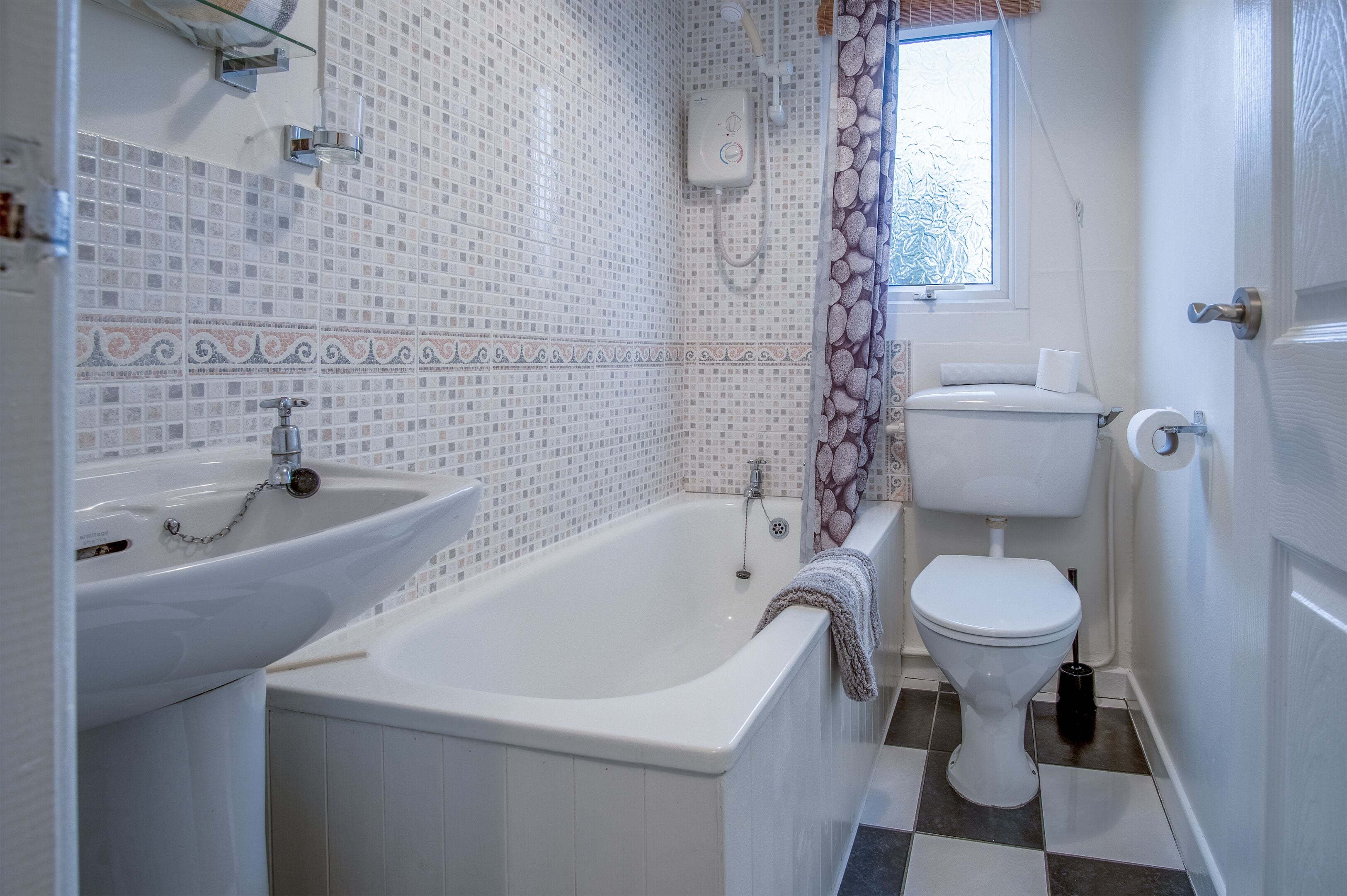 A bathroom with a bathtub, sink, toilet, and a window with a curtain.