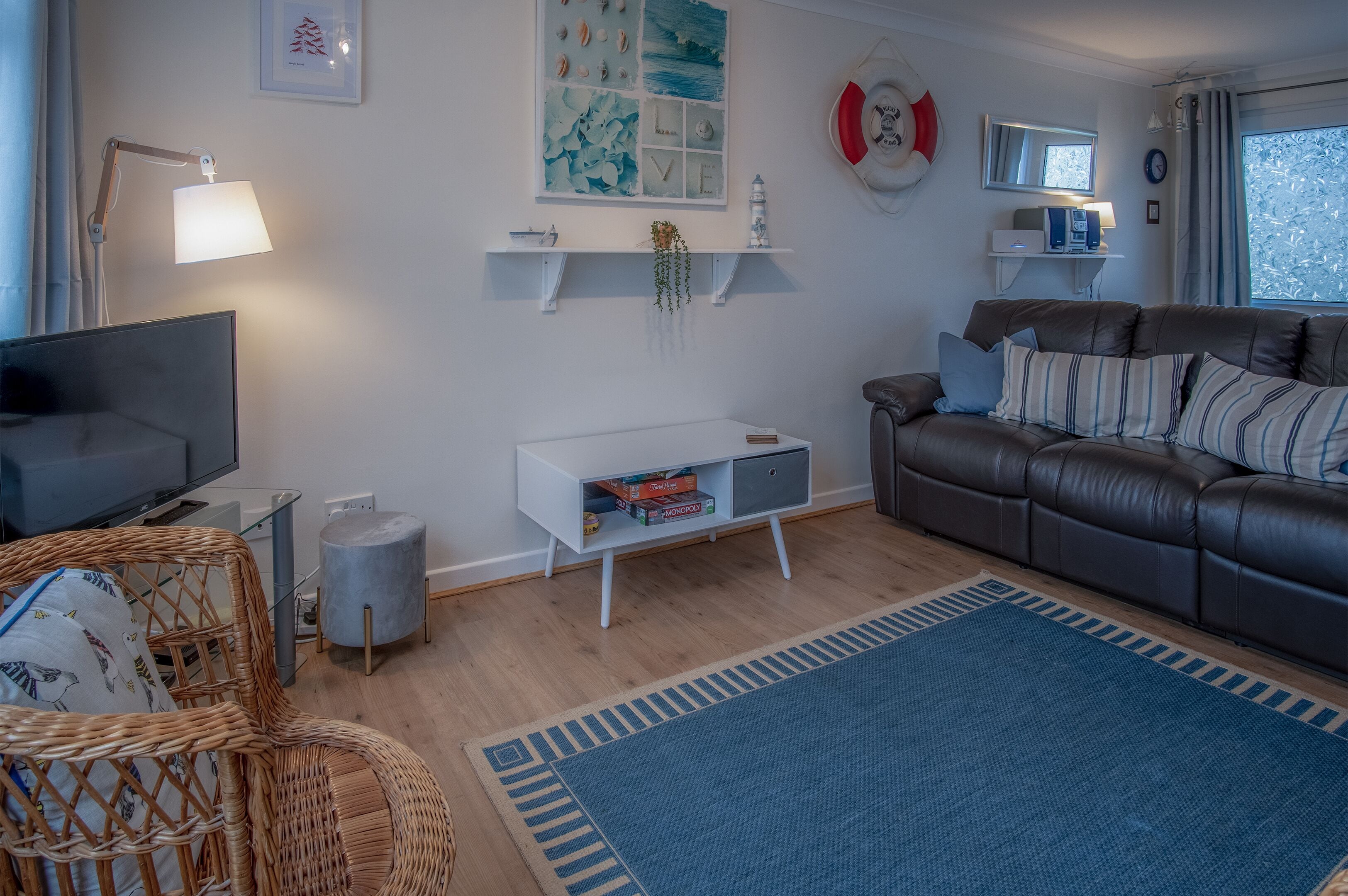 En moderne stue med en lædersofa, et fladskærms-tv, en fletstol og en blå måtte.