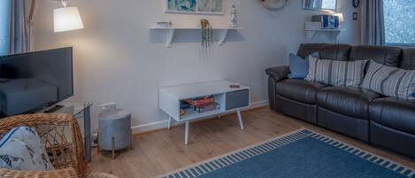 A modern living room with a leather sofa, a flat-screen TV, a wicker chair, and a blue rug.