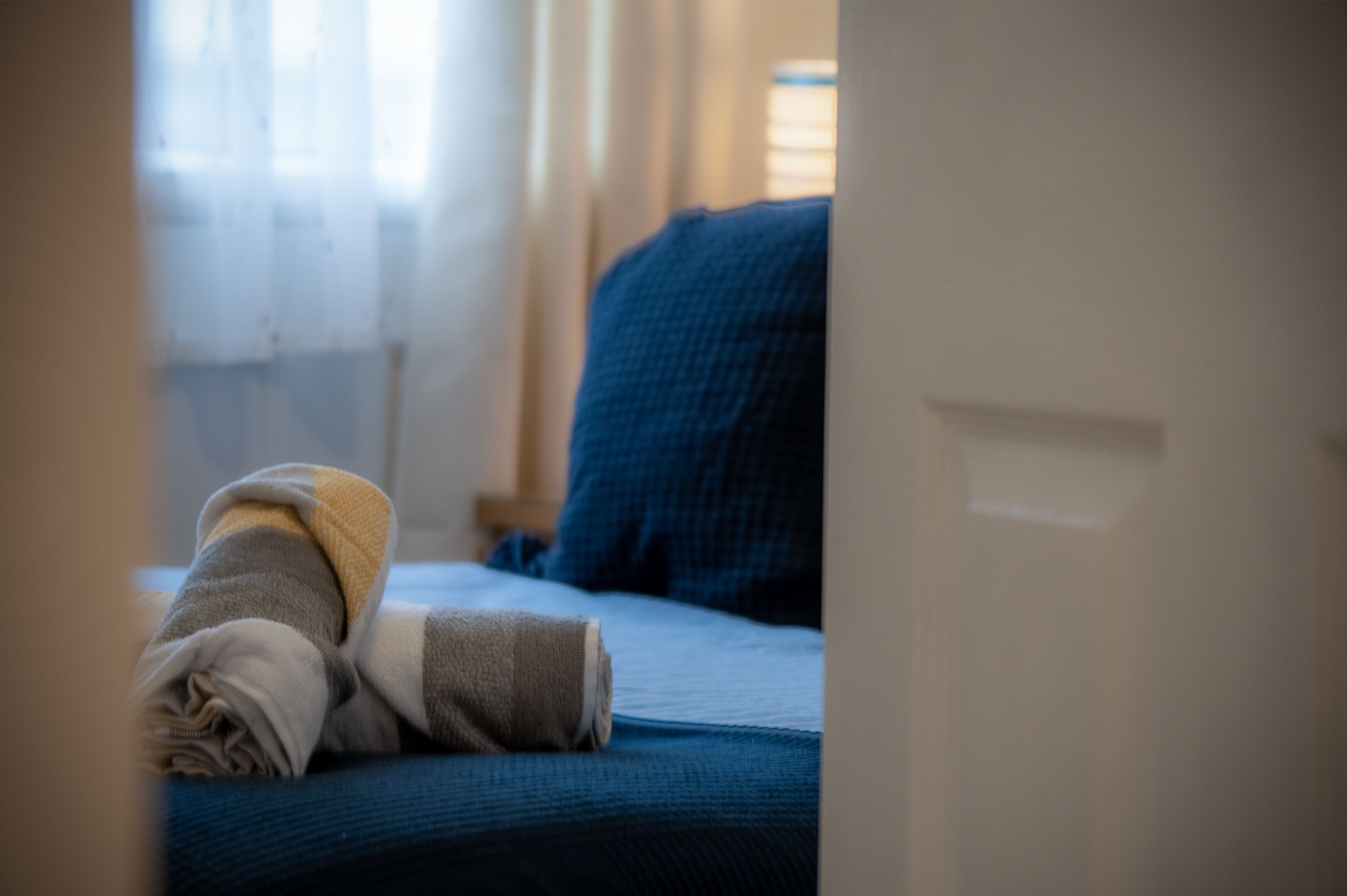 Un letto con una coperta blu e un asciugamano arrotolato.