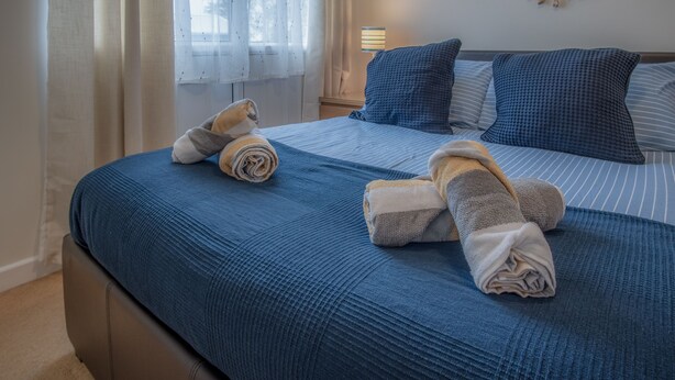 A neatly made bed with blue bedding and two towels folded on top. - Trewent Park - 2 Bed - Freshwater East (Pembroke)