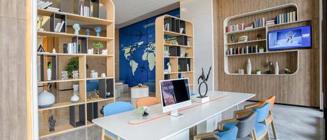 A modern library with a large world map on the wall, multiple bookshelves, a desk with a computer, and blue chairs.