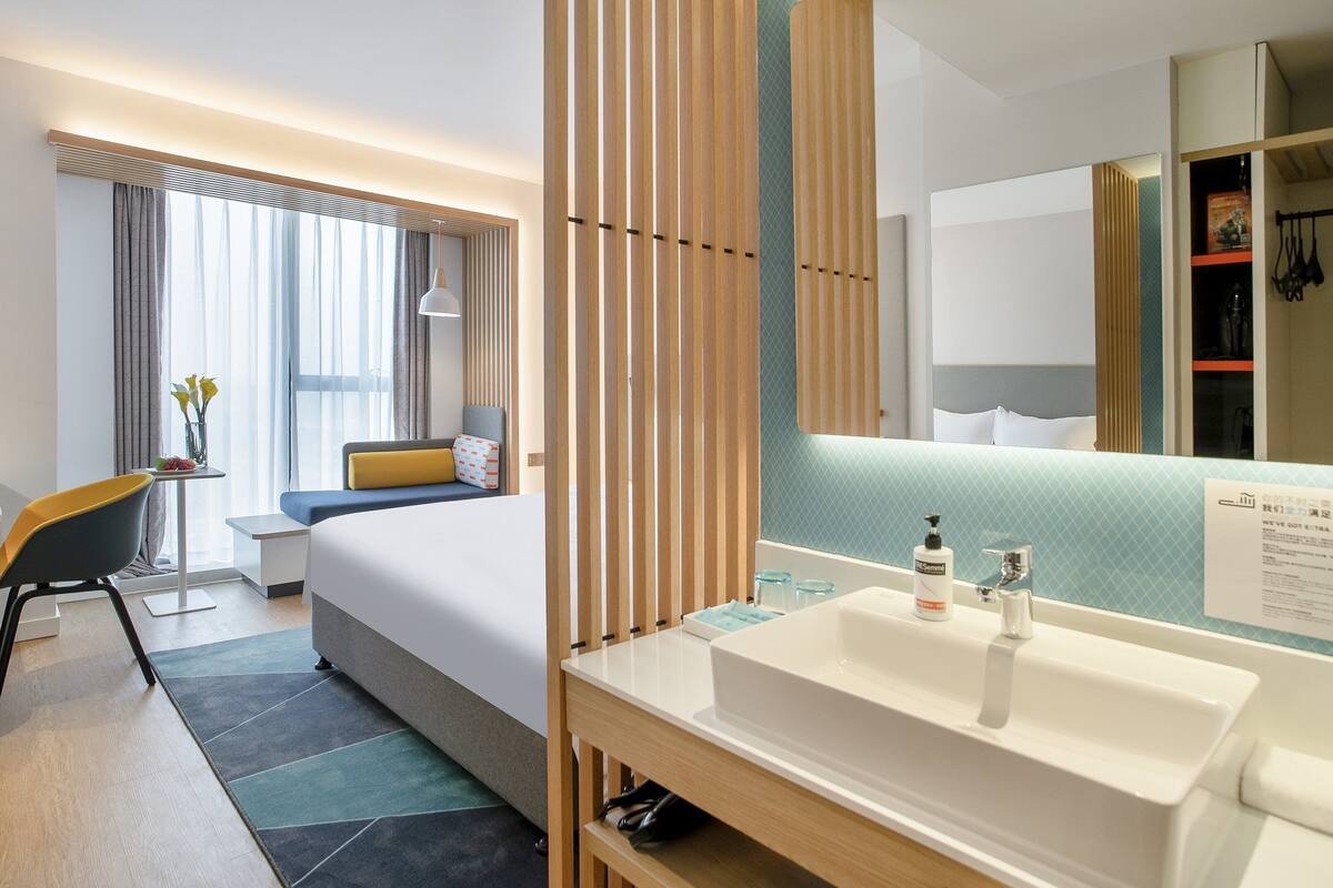 A modern hotel room with a bed, bedside table, chair, and a large mirror.