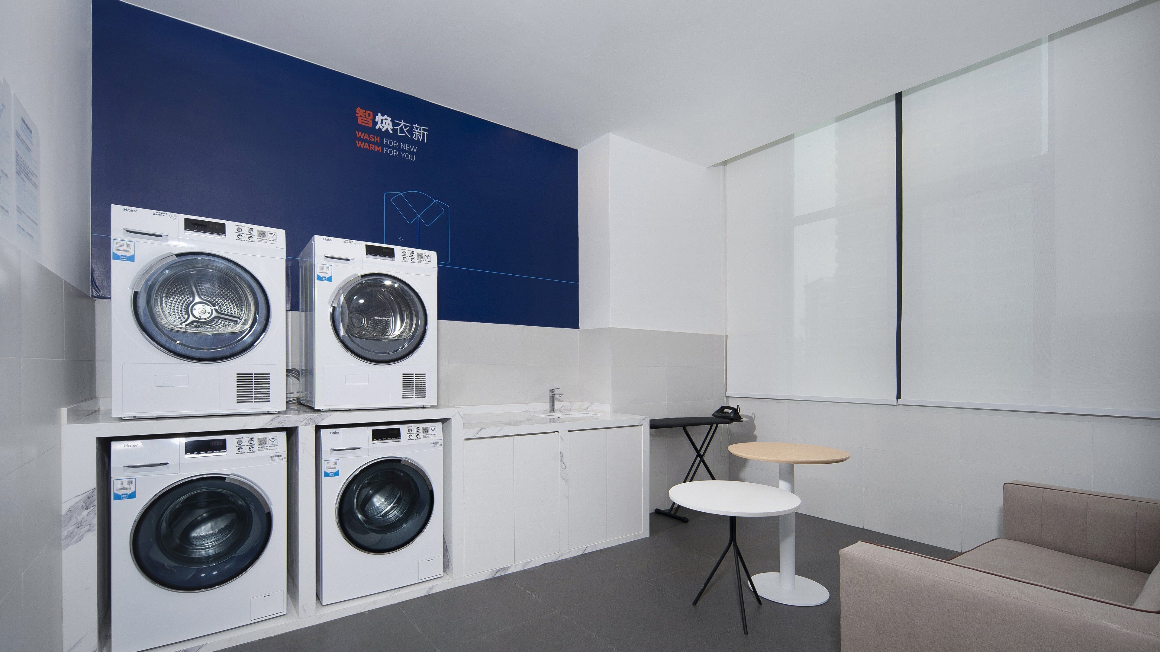 A modern laundry facility with multiple Haier washing machines, a small table, and a couch.