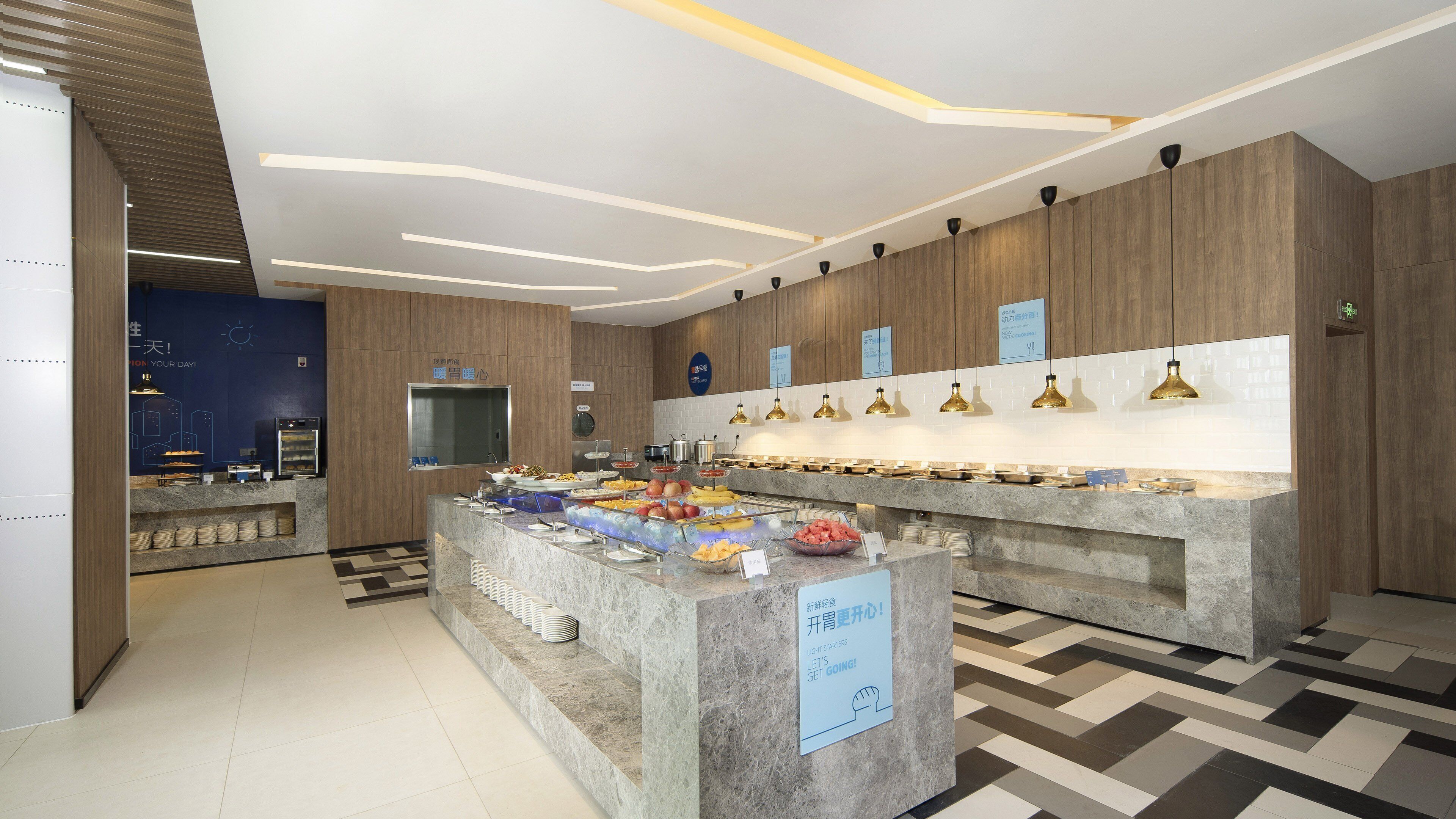A modern breakfast buffet area with a variety of food options, a digital clock, and a sign encouraging light starters.