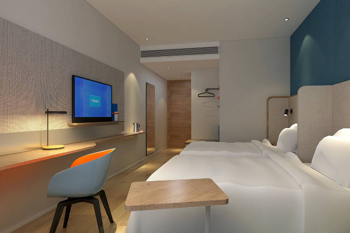 A modern hotel room with a bed, a desk with a chair, a television, and a wardrobe.