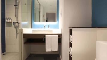 Un baño moderno con ducha, lavamanos con espejo y un perchero para toallas.