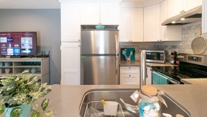 A modern kitchen with white cabinets, a stainless steel refrigerator, a microwave, and a built-in oven.