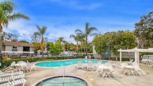 A swimming pool with lounge chairs and a hot tub, surrounded by palm trees and a clear sky.