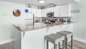 Uma cozinha moderna com armários brancos, bancada de granito, micro-ondas embutido e um balcão com dois bancos.