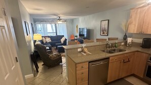 A modern kitchen with a central island, wooden cabinets, and a dishwasher. - First Floor Beach Club Villa with Marsh Views - Walk to the Beach! (Saint Helena Island)