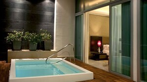 Ein moderner Innenpool mit einer Holzdielen-Terrasse, einer Sitzecke mit einer roten Lampe und Blick auf einen Raum durch Glastüren.