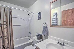 Een badkamer met een bad, toilet, wastafel en een spiegel met handdoekhouder.