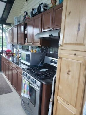 A kitchen with wooden cabinets, a gas stove, an oven, and a microwave.