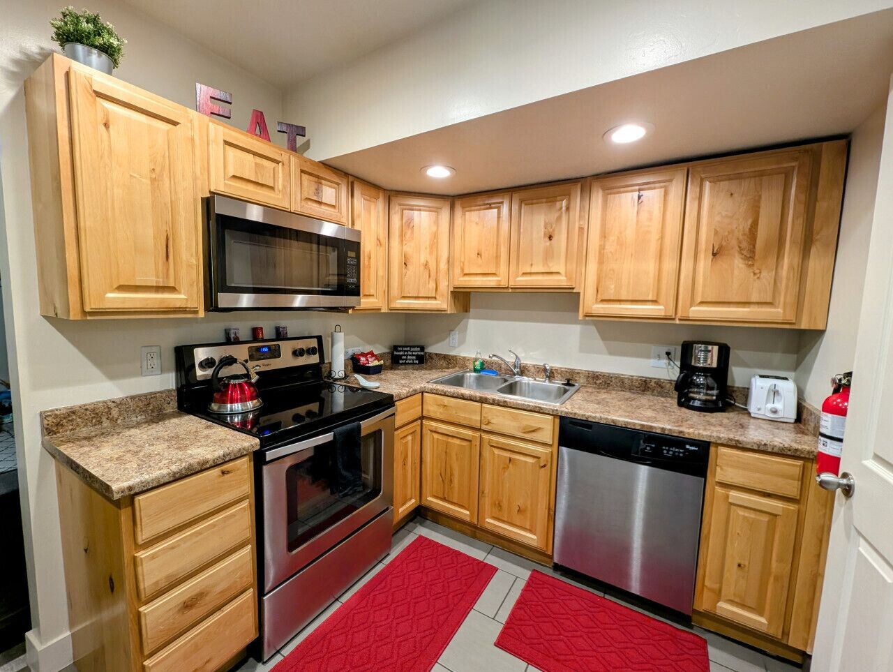 A compact kitchen with wooden cabinets, stainless steel appliances, and a red rug.