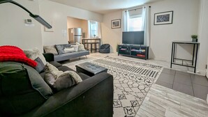 Un salon avec un canapé, un téléviseur, une table basse et un tapis à motifs.