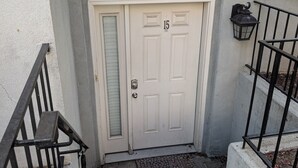 Un immeuble résidentiel avec une porte blanche portant le numéro 15, une rambarde en métal noir et une petite lanterne noire fixée au mur.