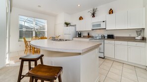 Uma cozinha moderna com armários brancos, uma ilha central e uma área de refeições com cadeiras de madeira.