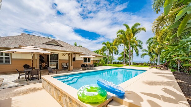 Una piscina con borde de piedra, una silla de descanso y una mesa con sillas.