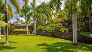 Un jardín bien cuidado con palmeras, una hamaca y un muro de piedra.