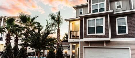 A multi-story residential building with a garage, a balcony, and a pool in the background.