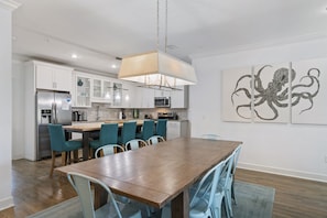 Una cocina moderna con armarios blancos, una mesa de comedor de madera, sillas color turquesa y una lámpara colgante.