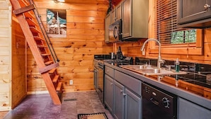 L’intérieur d’une cabane en bois comprend une cuisine, un escalier en bois et une fenêtre avec des stores.