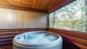 A hot tub in a wooden cabin with a view of trees through a window.
