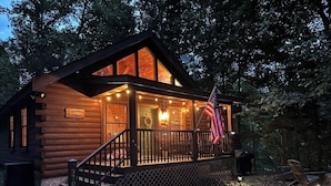 Une cabane en rondins avec une véranda, des marches et un drapeau américain.