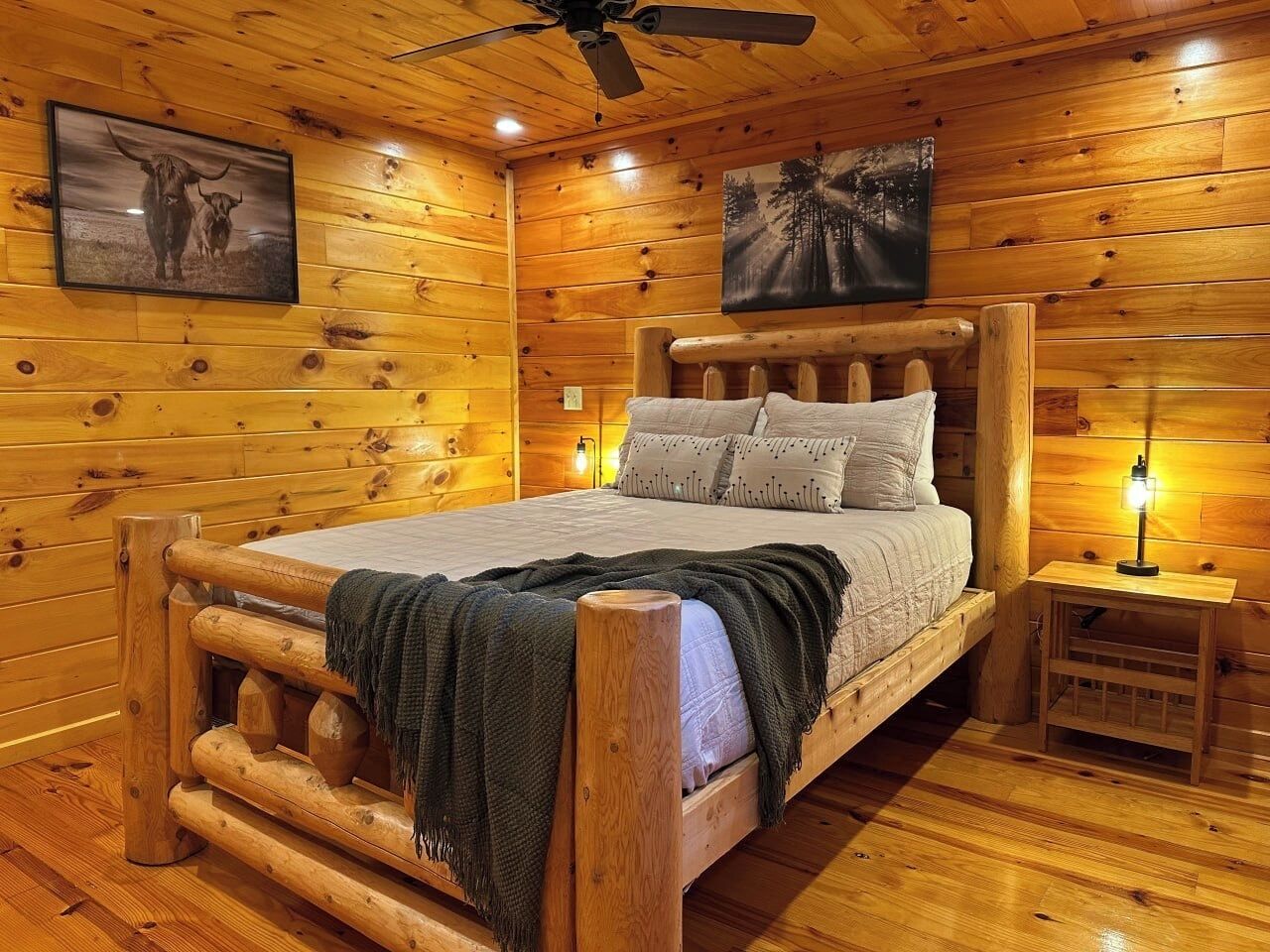 Camera da letto in una baita di legno, con un letto, un comodino, una ventola a soffitto e due quadri appesi al muro.