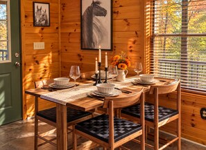A wooden interior with a dining table set for four, featuring a candle centerpiece, white plates, and black cushioned chairs. - ★ Prime Location ★ Fun Family Getaway ★  (Pigeon Forge)