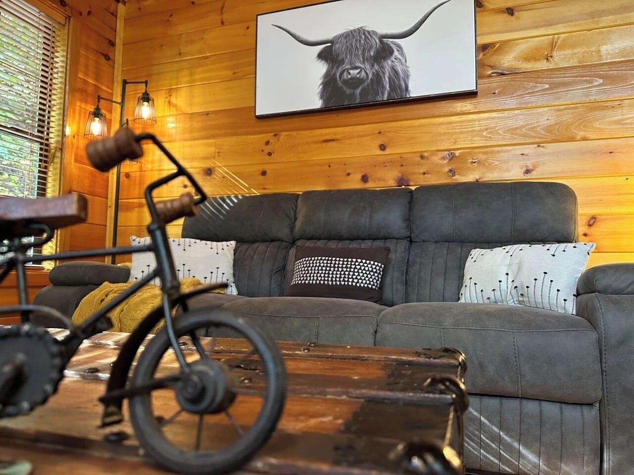 Un interior cálido de cabaña con un sofá, almohadones, una bicicleta y un cuadro en la pared.