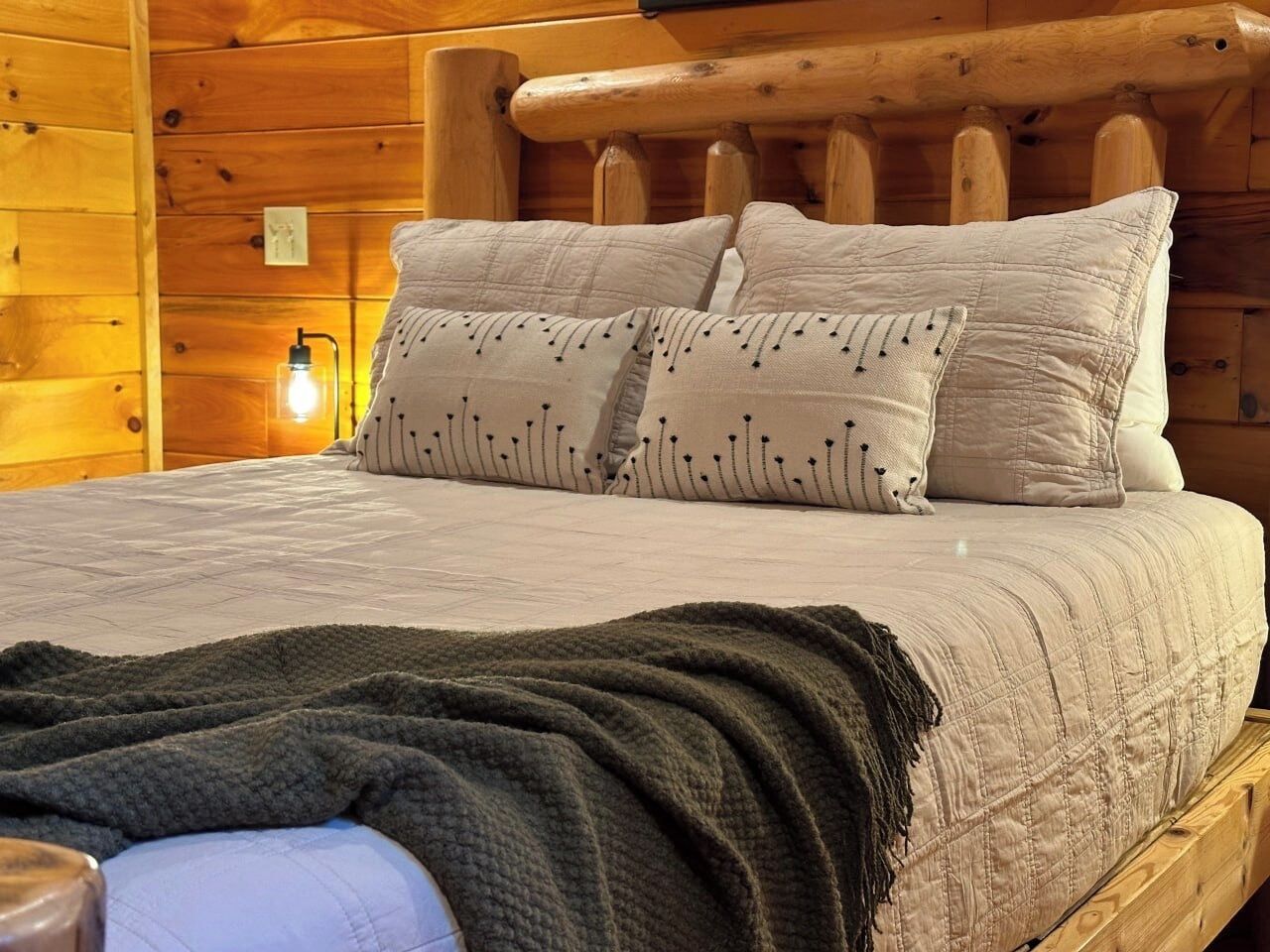 A wooden cabin-style bedroom with a bed, pillows, and a blanket.