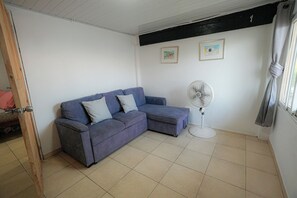 Une pièce avec un canapé bleu, un ventilateur sur pied et deux tableaux encadrés accrochés au mur.