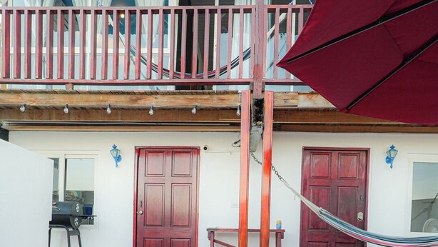 Une piscine aux carreaux bleus, un parasol rouge et une terrasse en bois avec un hamac.