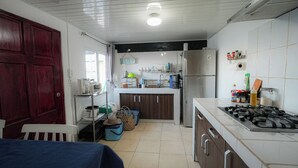 Une cuisine équipée d’une cuisinière, d’un réfrigérateur et de divers appareils électroménagers. On y trouve une table à manger recouverte d’une nappe bleue.