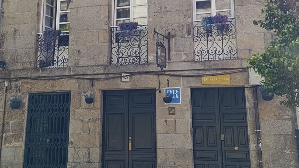 A two-story building with a stone facade, multiple windows, and black metal gates. - Casa Douro (Santiago de Compostela)