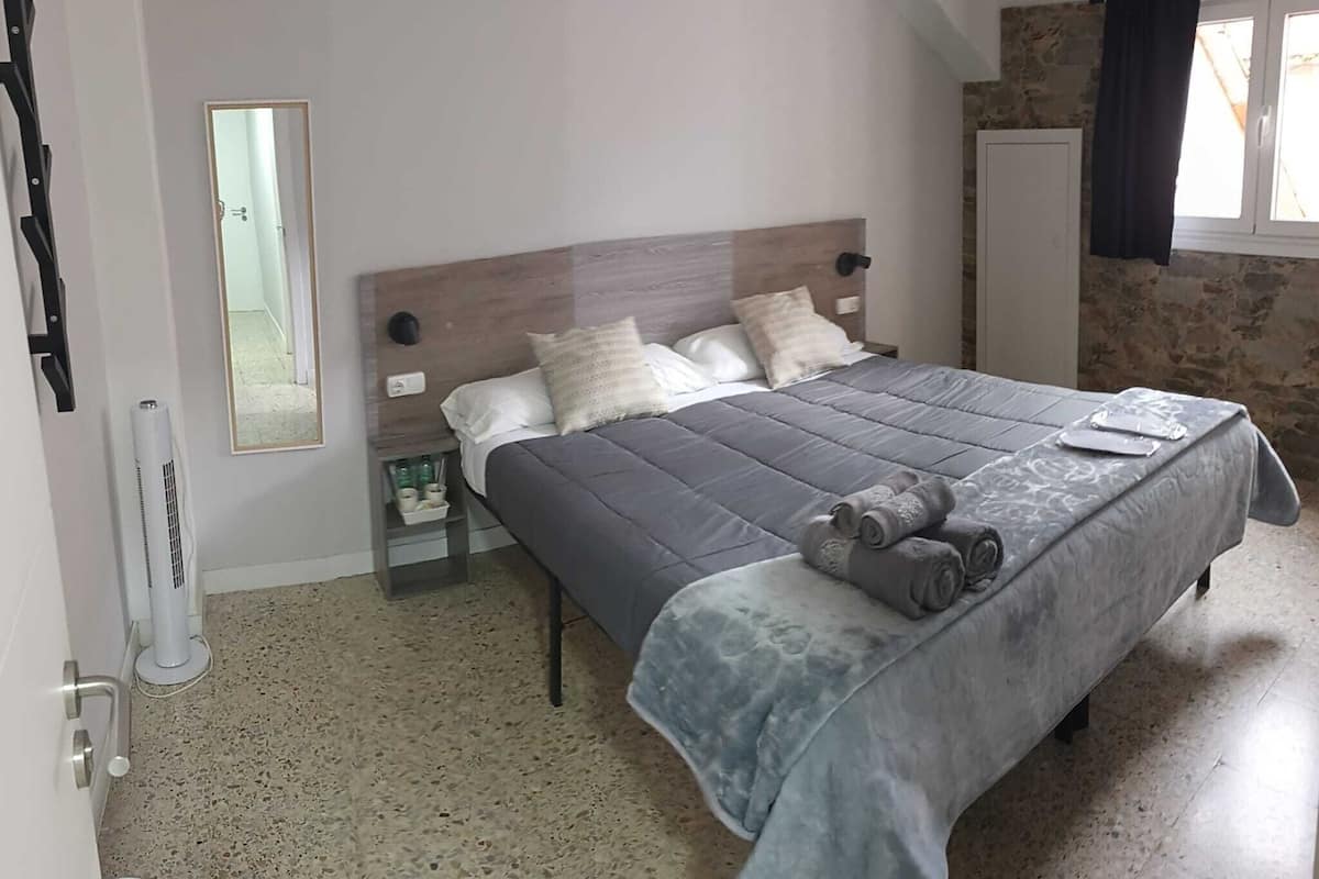 A bedroom with a bed, a nightstand, a mirror, a wardrobe, and a window with curtains.