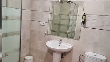A bathroom with a glass shower enclosure, a pedestal sink, a toilet, and a mirror above the sink.